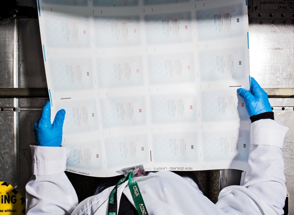 CBN employee wearing protective blue gloves pulls sheet of passport pages out of printer