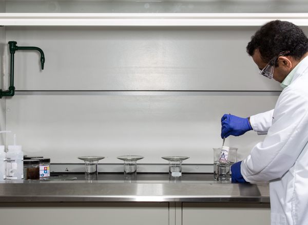 Un technicien de laboratoire CBN portant des lunettes de sécurité teste un billet de banque en le plaçant dans un liquide transparent