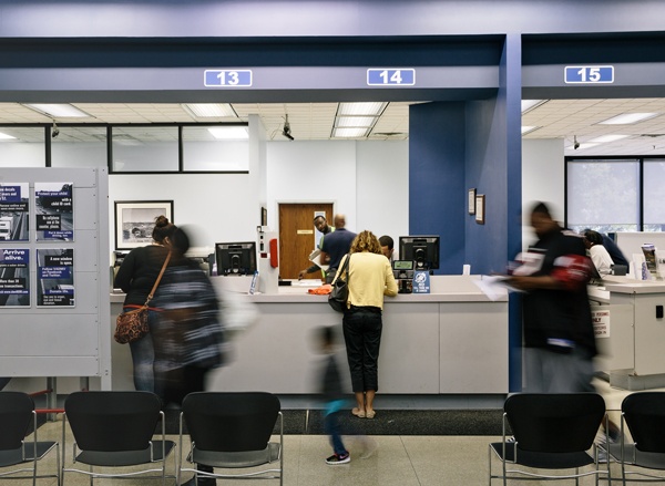 Woman stands in front of Driver and Motor Vehicle Department employee at help desk