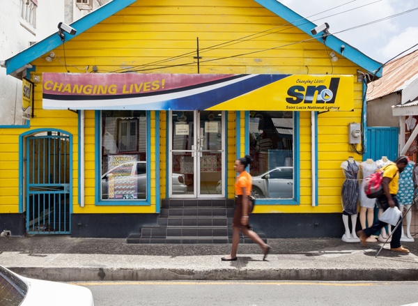 Mujer local camina delante de un terminal de lotería de color azul y amarillo en St. Lucia