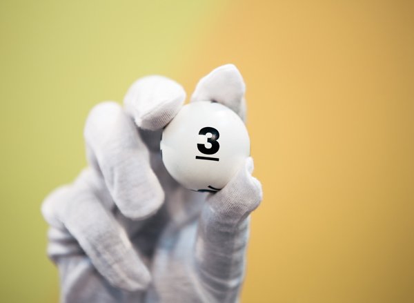 Une main gantée blanche tient une boule de loto, montrant le numéro trois