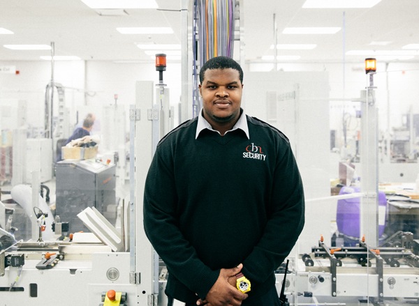 Un employé de CBN avec un uniforme de sécurité se tient devant une zone de production